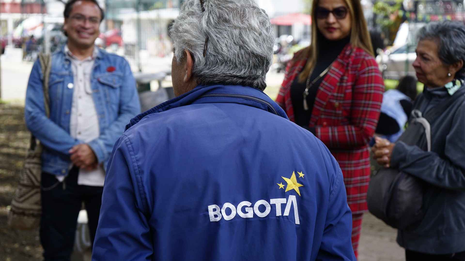  Descripción: Un hombre con una chaqueta azul con el logo de "Bogotá" y tres estrellas doradas en la espalda. 
