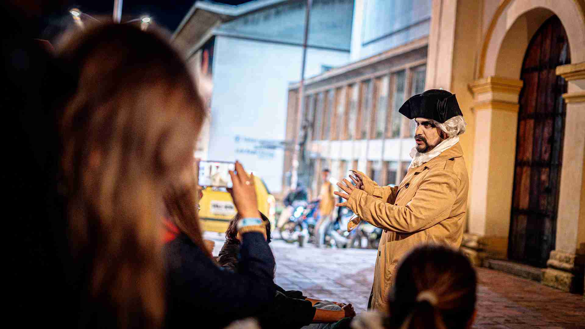 Un actor disfrazado de personaje histórico interactúa con el público en una calle, creando una atmósfera teatral.