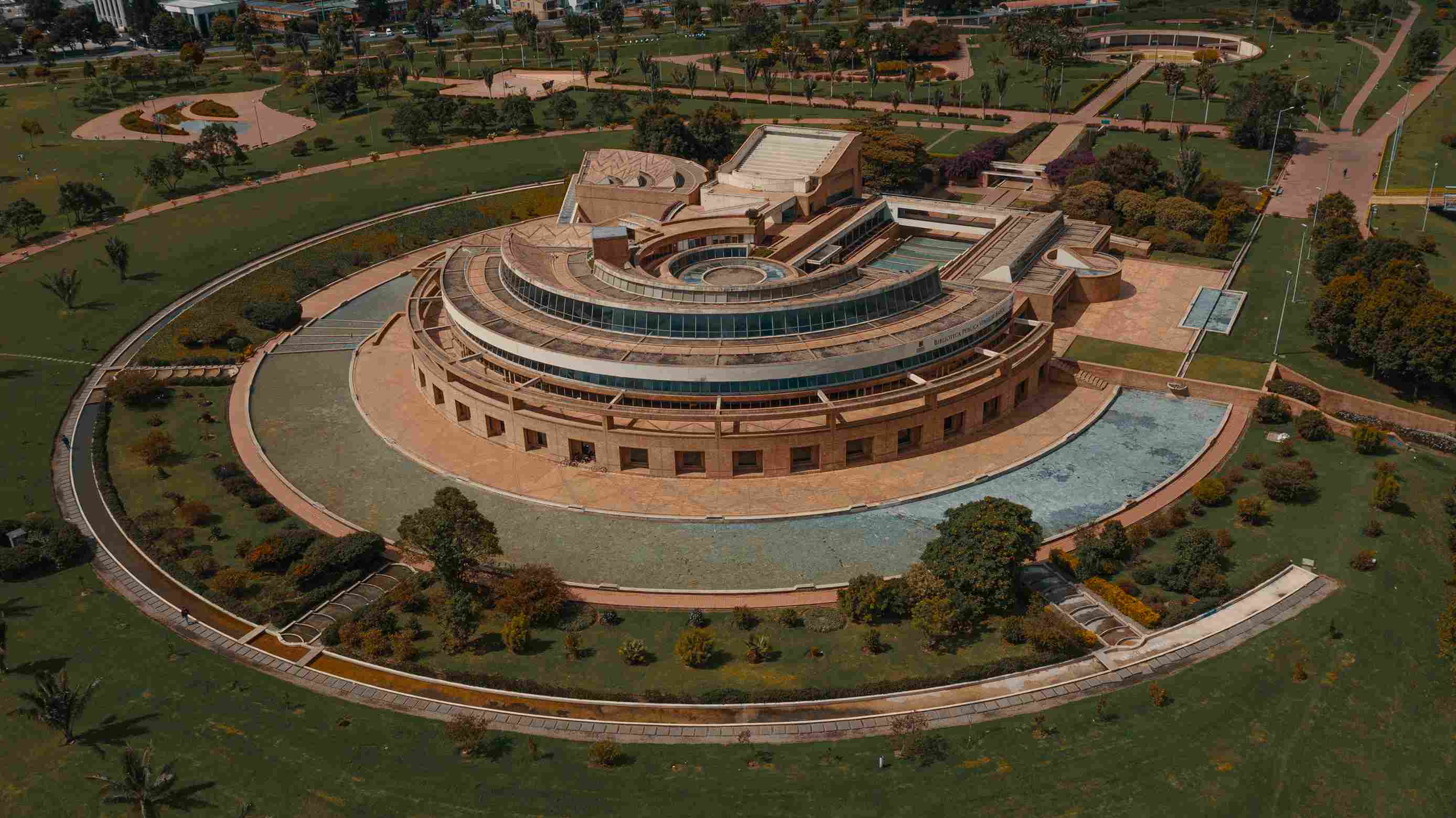 Aerial view of the circular Virgilio Barco Library building in the center of a park surrounded by trees and green areas. From above, the building resembles a spaceship on land.
