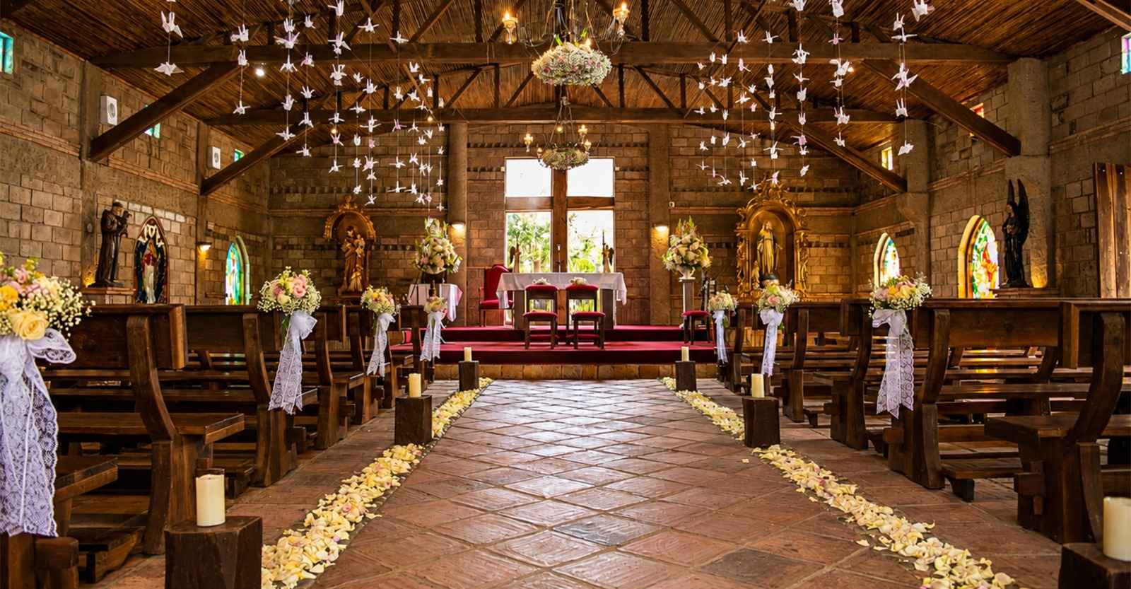 Una capilla de estilo rústico y acogedor, decorada con flores, velas y delicadas figuras de papel que realzan su belleza. La combinación de piedra, madera y luz cálida crea un escenario íntimo y romántico, perfecto para una ceremonia especial.