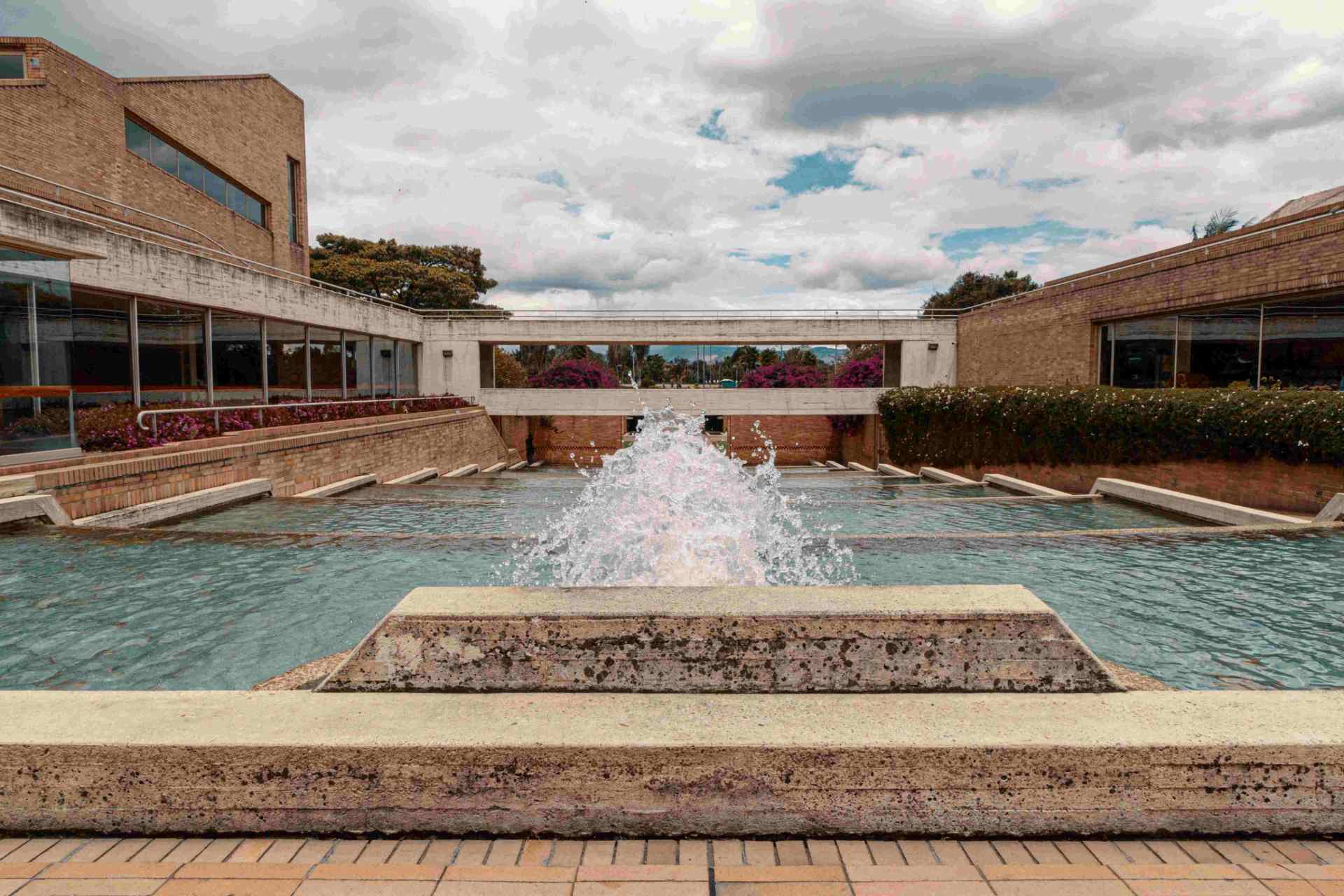 Biblioteca Virgilio Barco exterior de día con fuentes de agua, paredes de ladrillo y ventanales exteriores.
