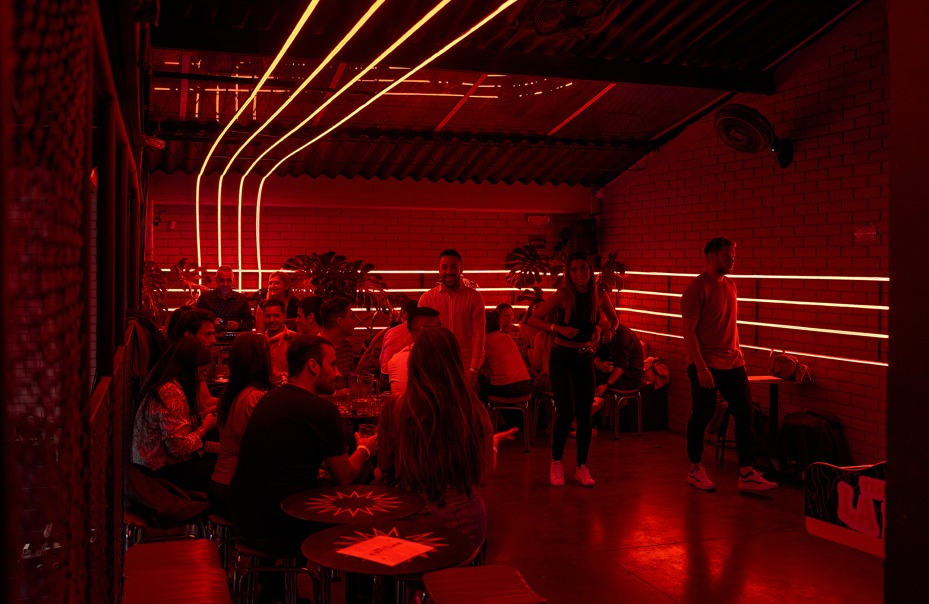 Un joven lanza una bola en una sala de juegos interior, rodeado por un grupo de amigos que observan la acción.