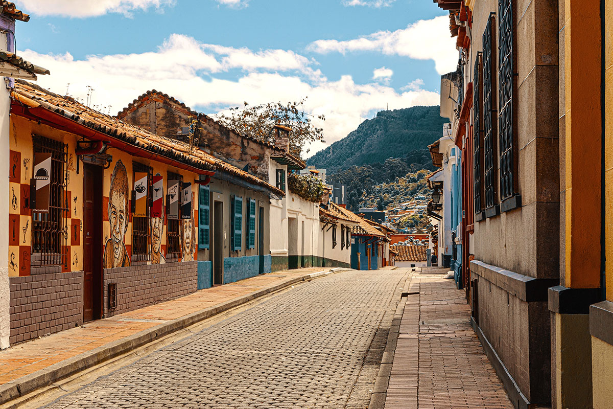 Calle vacía de La Candelaria con fachadas de casas antiguas de colores. ielo azul y montaña verde de Cerros Orientales.