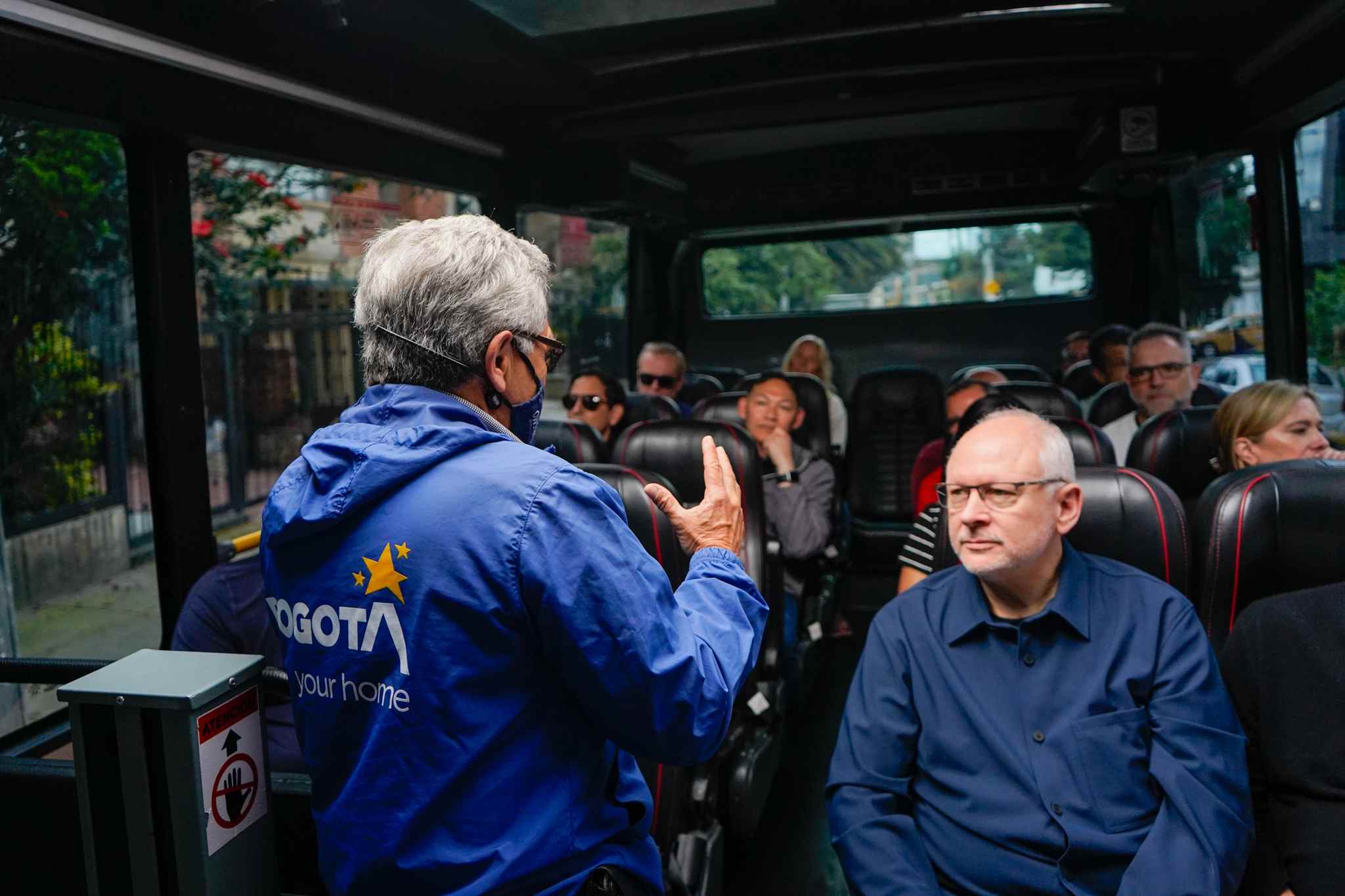 Guía turística conversa con visitantes durante un recorrido por Bogotá en un vehículo turístico