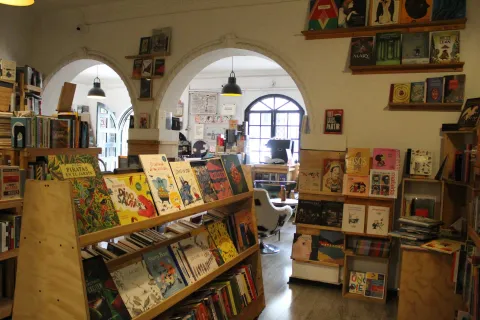 Garabato Libros, a room with bookshelves on the floor and walls packed with books. In the background, another room can be seen with a large window featuring geometric patterns and a door leading to the street.
