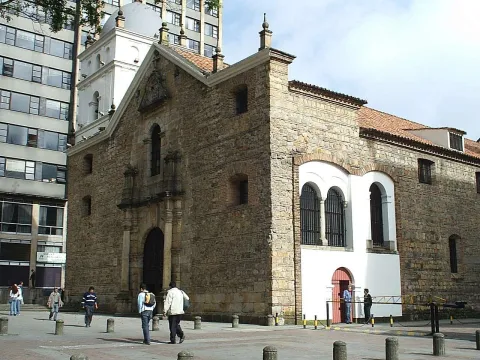 Templo de San Agustín colonial vista fachada y lateral izquierda, se observan gran puerta central, puerta lateral y ventanales. Al fono hay un edificio moderno. Algunas personas transitan por el frente.