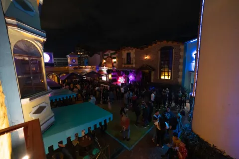 Theatron de noche en plazoleta interior con fachadas de castillos iluminadas y personas que bailan y conversan alrededor.