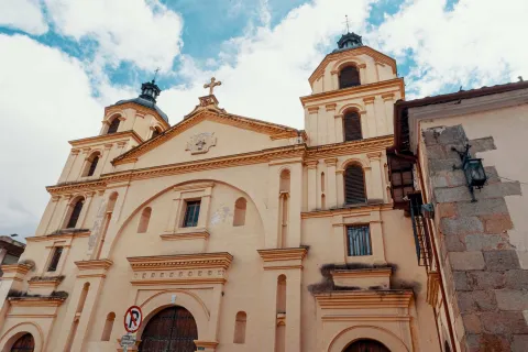 Iglesia de la Candelaria colonial de frente a su fachada, se ve desde la puerta de madera  con forma de óvalo hasta el techo coronado con una cruz y las torres izquierda y derecha con sendas cúpulas negras y cruces metálicas encima. 