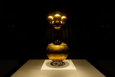 Gold Museum with the Poporo Quimbaya, an ancestral gold vessel inspired by the shape of a gourd. It features a filigree base with spiral designs, a braid at the beginning of its neck, and a top ornament with four spheres.
