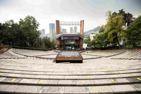 Open-air brick theater, daytime view. Steps leading to the stage are visible, covered by a roof, two brick columns, and a large sign reading ""Idartes.""