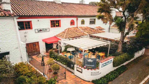 Vista aérea de un encantador restaurante de ladrillo blanco con techo de tejas, patio exterior cubierto y exuberante vegetación.