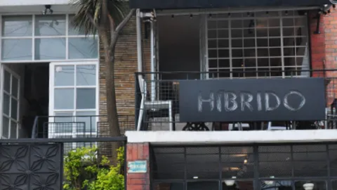 La fachada de un restaurante llamado "HIBRIDO" con una terraza, ventanales y un diseño moderno.