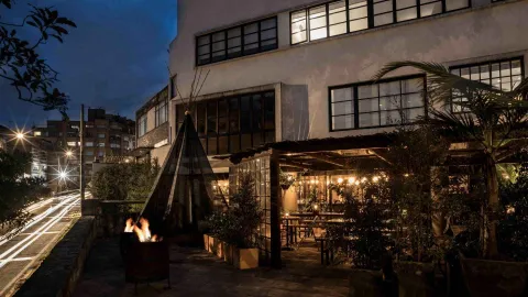 FOTO INDIO: Una terraza de restaurante por la noche, con un tipi, hoguera encendida y luces colgantes.