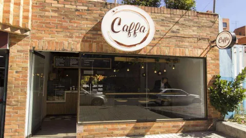 La fachada de ladrillo de la cafetería Caffa, con su logo circular, grandes ventanales y un reflejo de coche en el cristal.