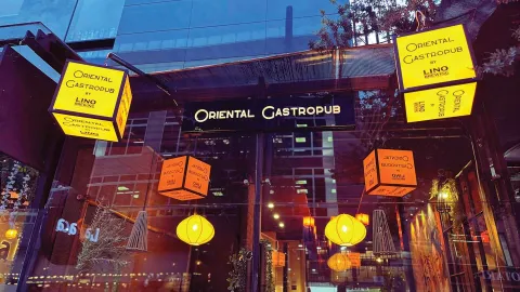 La fachada de un "Oriental Gastropub by Lino Brewing", con letreros iluminados y decoraciones colgantes que crean un ambiente acogedor al anochecer.