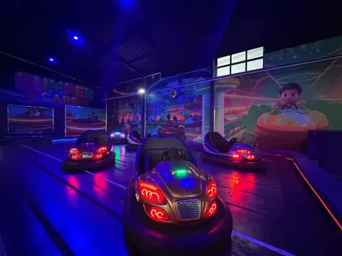 Tres carros chocones en un parque de atracciones. El lugar está oscuro y las paredes están pintadas con figuras infantiles en carros chocones.