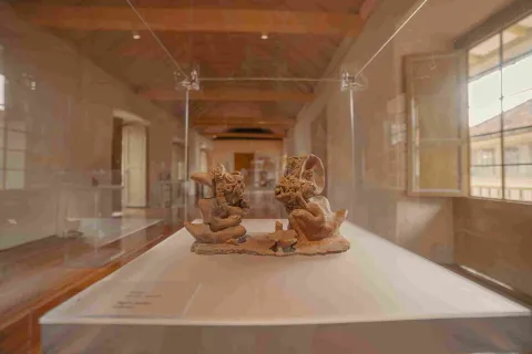 A ceramic piece in the shape of two men wearing animal skins is displayed in a glass case.