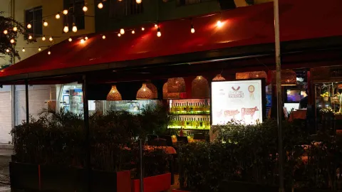 Un restaurante acogedor por la noche, iluminado con luces cálidas, toldos rojos y plantas en el exterior.