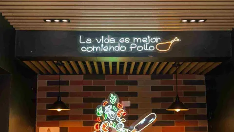  Un letrero de neón con la frase "La vida es mejor comiendo pollo" ilumina el techo de madera del restaurante.