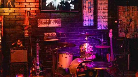 Un escenario de bar con batería, bajo y amplificadores bajo luces de colores, listo para una actuación.