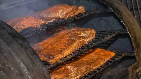 Costillas de cerdo asándose lentamente en una parrilla humeante, mostrando su delicioso ahumado.