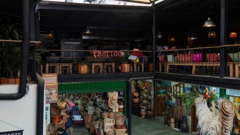 Fachada de un edificio con un restaurante llamado ""TESTIGO"" en el nivel superior y tiendas de artesanía en la planta baja. "