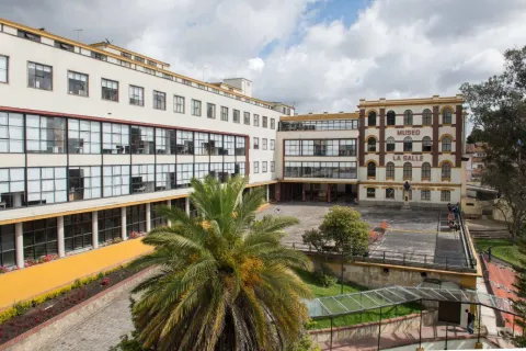 Façade of the La Salle Museum, an architectural complex that combines a historic brick building with arches and a modern structure featuring large windows. A spacious, open courtyard opens up in the center, surrounded by greenery and a palm tree that adds a touch of coolness. The partly cloudy sky frames the space, emphasizing the academic and cultural character of the place.