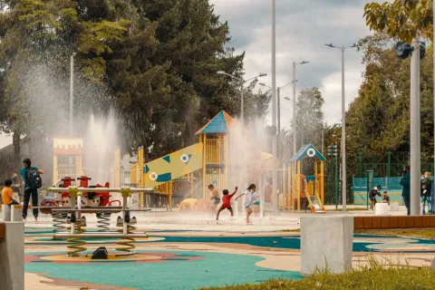 Children playing in the water in a park, laughing and enjoying a sunny day.