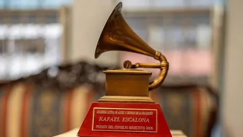 Trofeo con forma de gramófono en acabado dorado, montado sobre una base roja con una placa conmemorativa que menciona a Rafael Escalona y un premio otorgado en 2006. El objeto está exhibido en un espacio interior, con fondo desenfocado que sugiere una sala de exposición o museo.