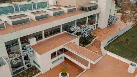 Vista aérea de un gran centro cultural moderno rodeado de zonas verdes y una ciudad al fondo.