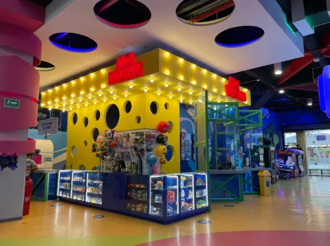 Mostrador de premios con vitrinas iluminadas en un parque de entretenimiento interior, rodeado de juegos y decoración colorida.