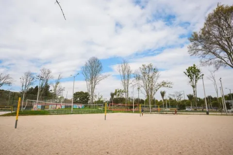 A beach volleyball court stretches out in a natural, open environment, surrounded by trees and recreational areas.