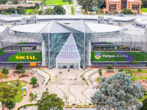 Vista aérea del centro comercial Parque La Colina en Bogotá, rodeado de zonas verdes, plazas peatonales y edificios urbanos.
