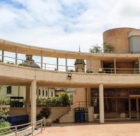 Vista del Centro Cultural Gabriel García Márquez en Bogotá, con sus característicos corredores curvos de concreto y ladrillo diseñados por Rogelio Salmona. Al fondo se observan elementos arquitectónicos del centro histórico de La Candelaria bajo un cielo parcialmente nublado.
