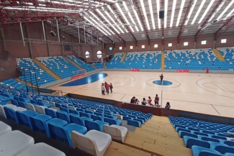 Interior view of the Cayetano Cañizares Coliseum, a modern sports venue with a large multipurpose court and blue bleachers, designed for competitions, training sessions, and large-scale events in Bogotá.