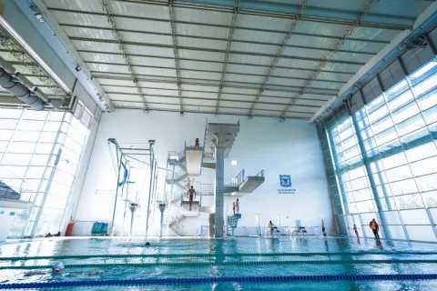 Vista interior del Complejo Acuático de Bogotá con piscina cubierta y plataforma de clavados de varios niveles, un escenario de alto rendimiento diseñado para la práctica y competencia de deportes acuáticos.