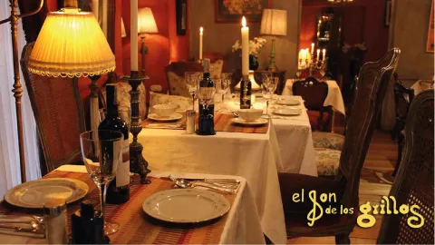 Mesa de restaurante con mantel blanco, copas de cristal, botellas de vino y candelabros con velas encendidas.