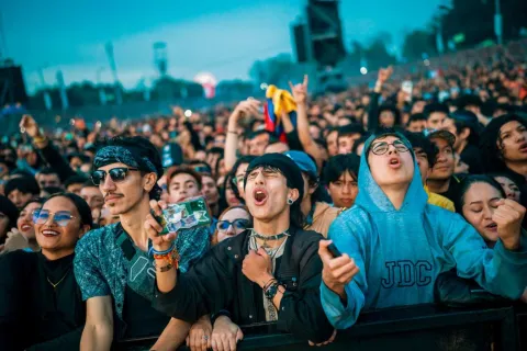 Multitud de jóvenes en un concierto al aire libre cantando y levantando las manos cerca del escenario.