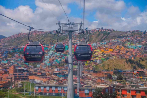TransMiCable cable cars gliding over colorful hillside homes in Ciudad Bolívar with mountains in the background