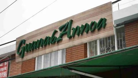 Letrero de madera con letras verdes en relieve con el nombre Guanab Annoa en la fachada del local. 