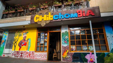 Foto 1: Fachada colorida con el letrero Chibchombia, murales artísticos folclóricos y ventanales con marcos de madera.