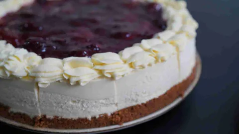 Cheesecake entero sobre base de galleta, decorado con crema chantilly y cobertura de mermelada de frutos rojos. 