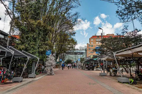 Zona G, con restaurantes y terrazas a ambos lados de una amplia vía peatonal, rodeada de árboles y edificios de ladrillo.