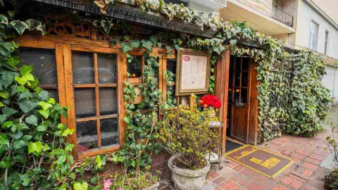 Foto 4: Fachada de estilo rústico cubierta de plantas trepadoras, ventanas de madera y letrero de entrada al restaurante.