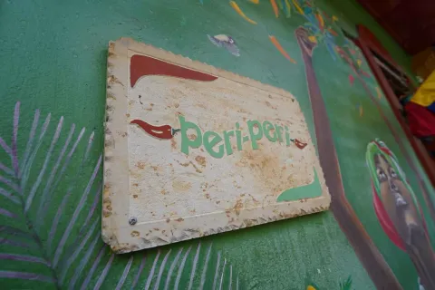 Foto 5: Placa de madera rústica tallada con el nombre del restaurante Peri Peri sobre una pared pintada de verde. 