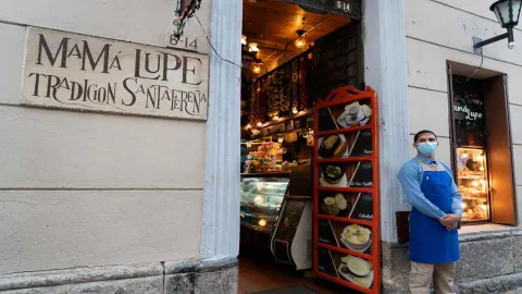 Foto 2: Plano medio de la entrada con placa de Mamá Lupe Tradición Santafereña, menú en marco rojo y empleado junto al portal. 