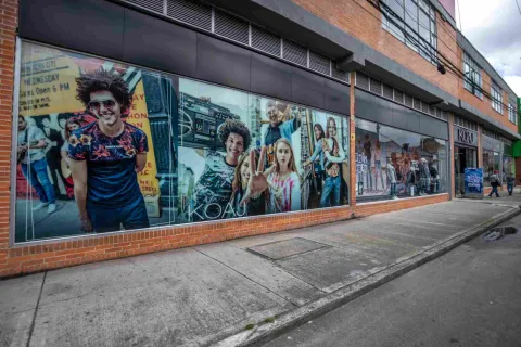 La fachada de una de las tiendas del Floresta Outlet luce amplios ventanales con coloridas campañas publicitarias, mientras la arquitectura en ladrillo y los amplios andenes acompañan el recorrido exterior del centro comercial.