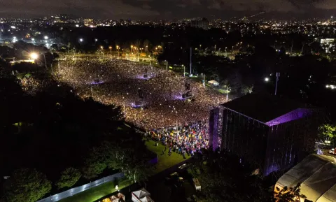 Vista aérea de un multitudinario concierto nocturno en parque, con miles de personas frente al escenario y la ciudad iluminada al fondo. Foto cortesía de facebook.com/rockalparquebogota/