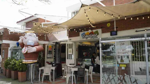 Fachada del local Riquísimo con terraza exterior, mesas, toldo con guirnaldas de luces y una figura inflable de personaje.