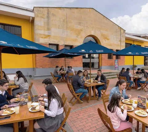 Terraza gastronómica del Mercado de la Concordia en Bogotá, con mesas al aire libre, sombrillas y visitantes disfrutando de diferentes platos.